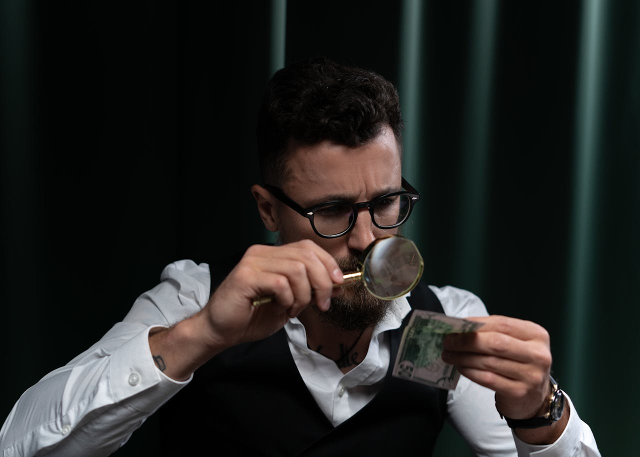Focused adult inspecting a banknote closely with a magnifying glass indoors.